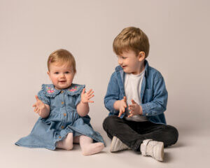 older boy wearing a blue denim shirt and white top and green trousers and sitting on the floor enjoying her photoshoot with a great family photographer in Belfast