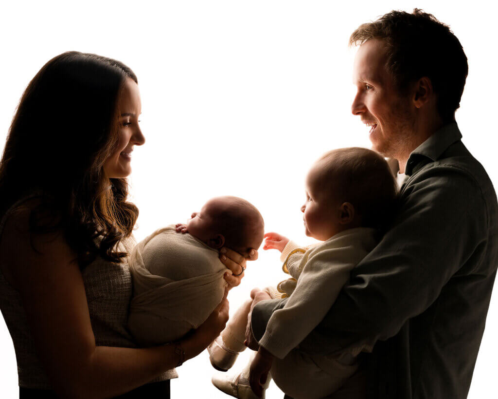 Mum and dad holding their toddler and baby on a white background by the best newborn photographer in Belfast