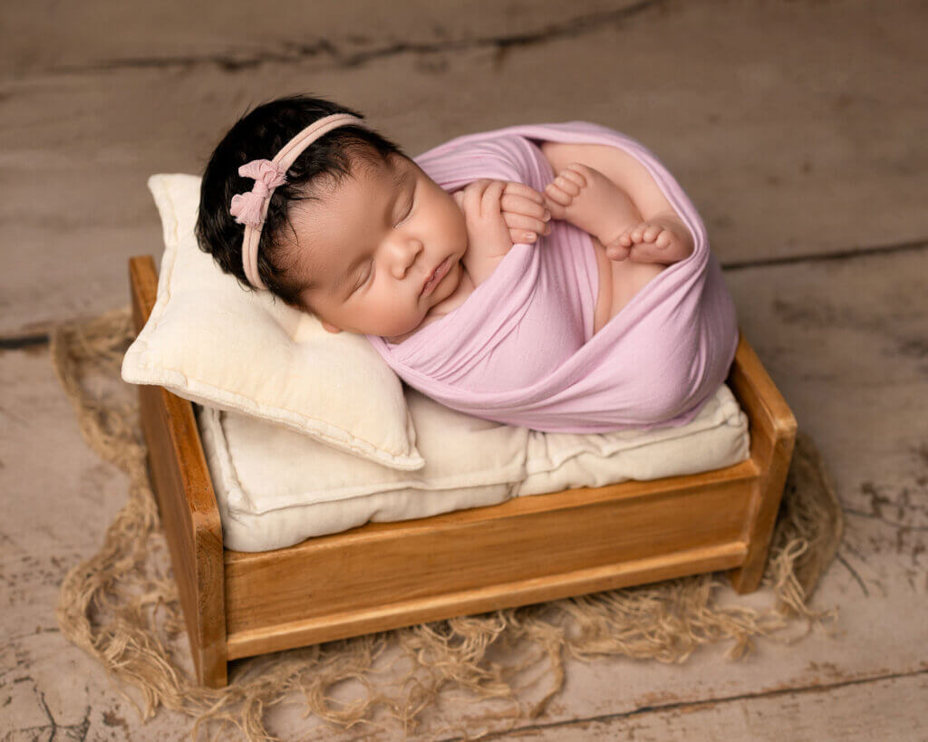 baby girl swaddled in pink and lying on a wooden bed by the best newborn photographer in Belfast