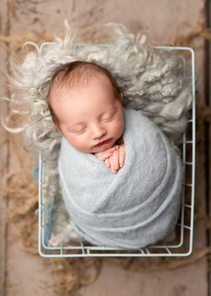 baby boy wrapped up and sleeping in a box by the best newborn photographer in Belfast