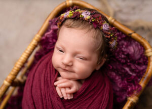 newborn baby wrapped in red with a floral headband on by newborn photographer in Belfast at her autumn newborn photoshoot